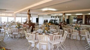 Un salón de banquetes con mesas redondas dispuestas para comer, rodeado de sillas blancas.
