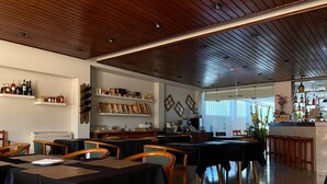 Un restaurante con techo de madera, mesas con manteles negros y estantes con botellas y bolsas.