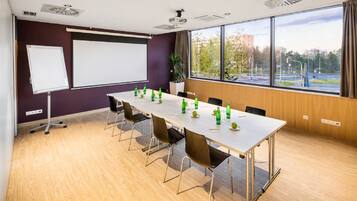 A conference room with a long table, chairs, a whiteboard, and a projector screen.
