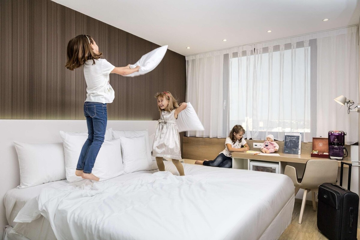 Quarto de hotel com cama, escrivaninha, cadeira, luminária e cafeteira.