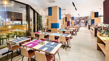 En moderne restaurant med flere borde og stole, store vinduer og udsigt til gaden.