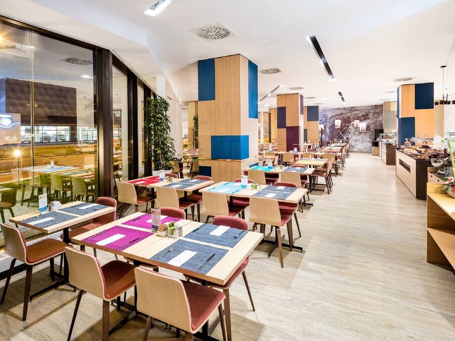Un restaurante moderno con varias mesas y sillas, ventanas amplias y vistas a la calle.