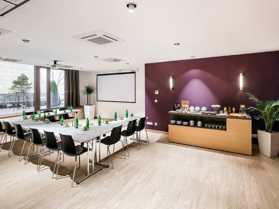 A conference room with a long table, black chairs, a whiteboard, and a reception area with a counter and plants.