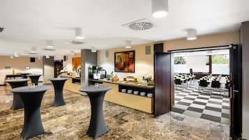 A modern hotel lobby with round tables, a reception desk, and a checkered floor.
