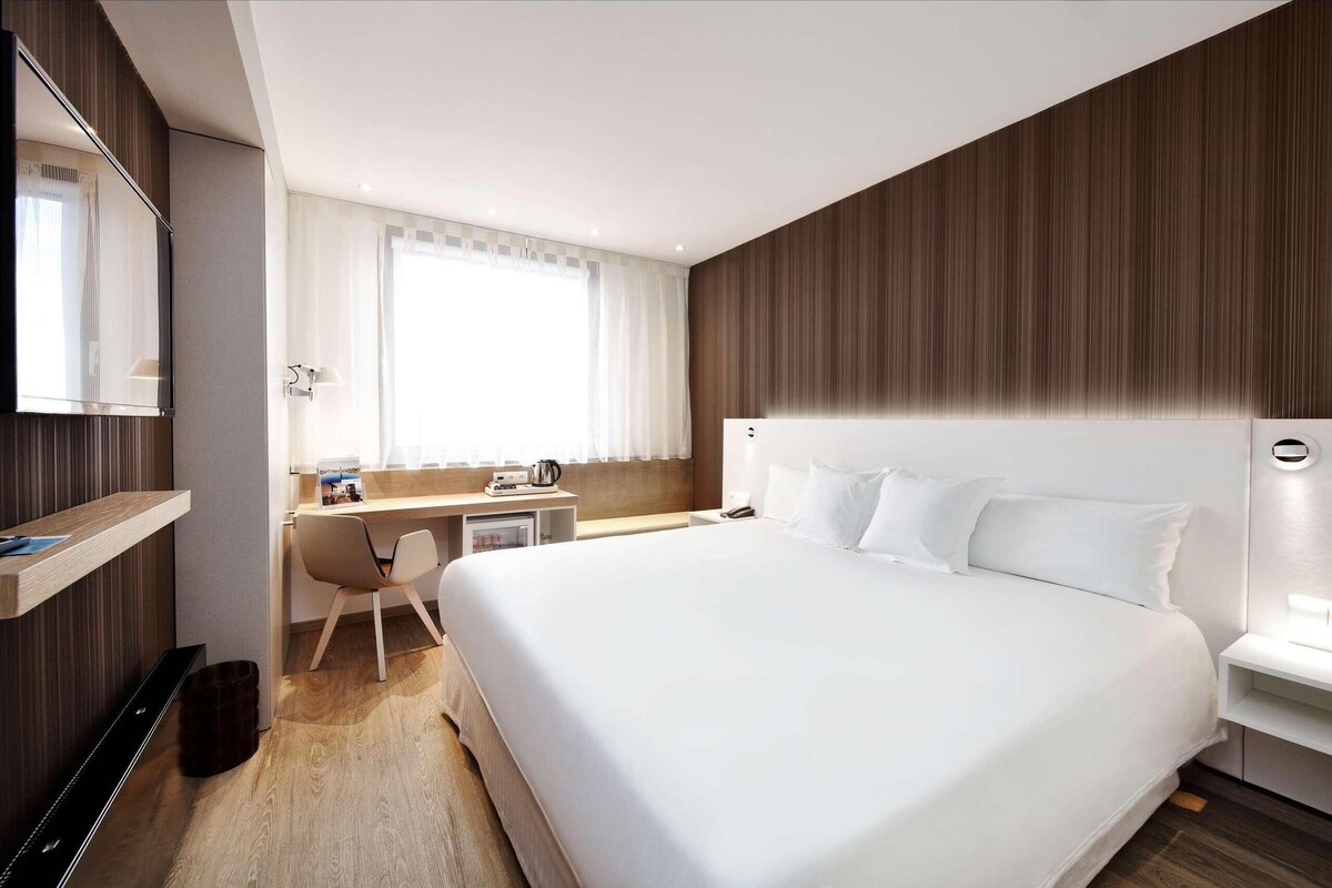 Quarto de hotel moderno com uma cama grande, uma escrivaninha e uma cadeira.