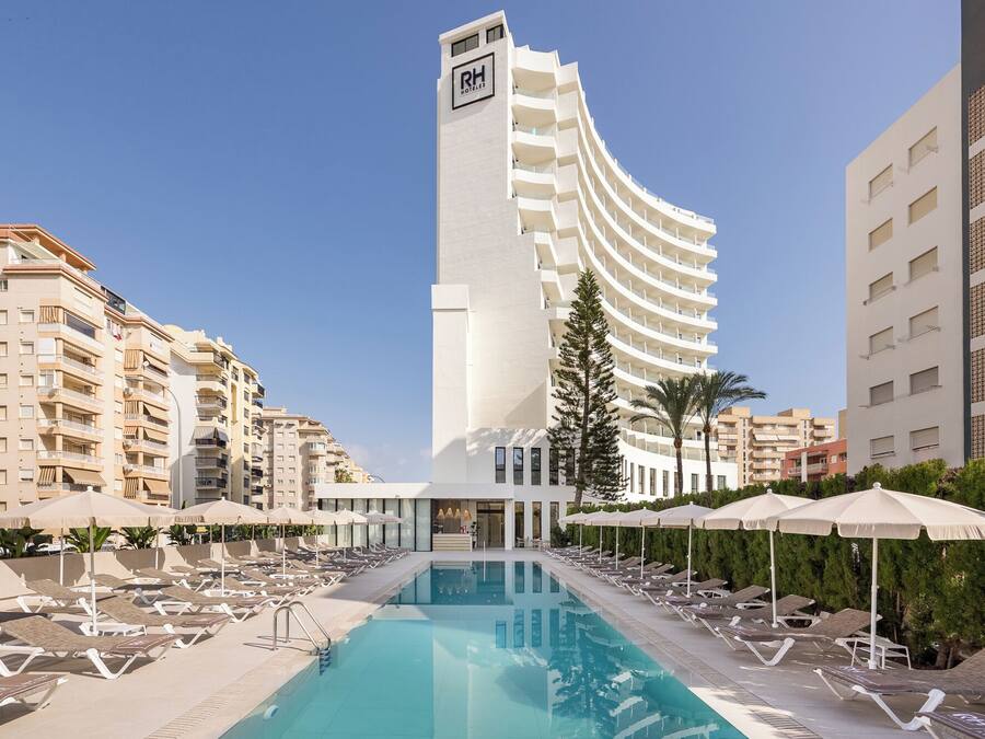 Un hotel con zona de piscina, tumbonas y un edificio alto con el nombre del hotel.