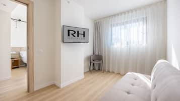Una habitación de hotel moderna con un ventanal grande, un sofá, una silla y un cartel de RH HOTELS.
