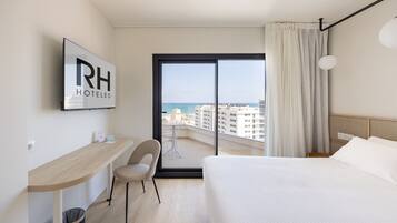 Ein Hotelzimmer mit Bett, Schreibtisch, Stuhl und Meerblick, mit einem Schild mit der Aufschrift 'RH HOTELS'.