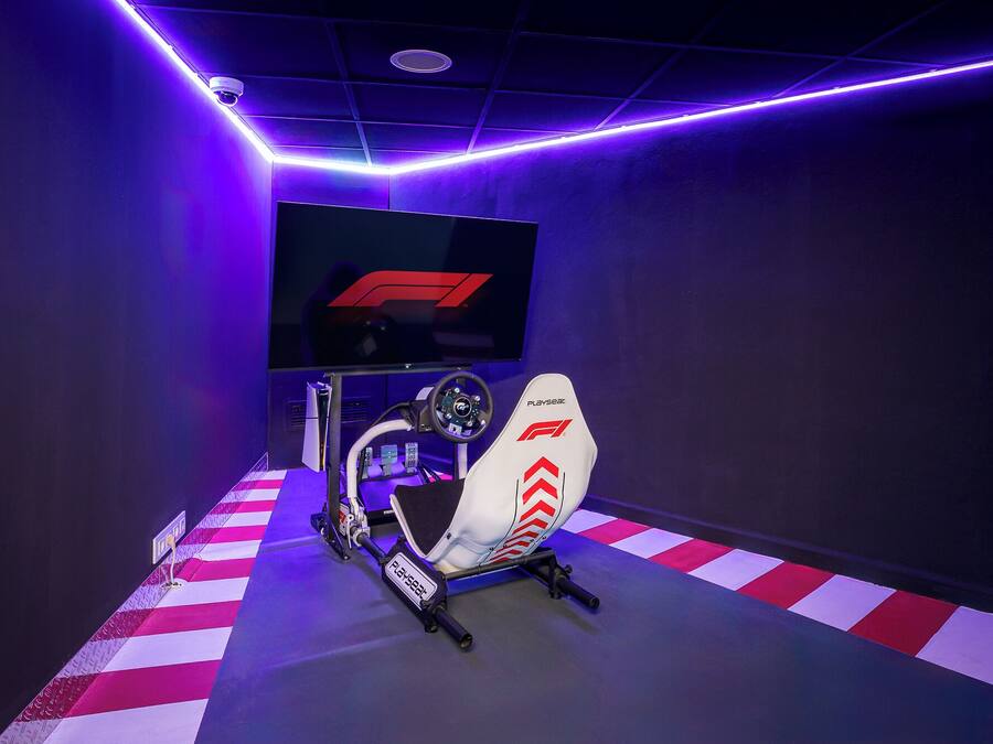 A racing simulator setup with a Playseat racing seat, steering wheel, and a monitor displaying a racing game.
