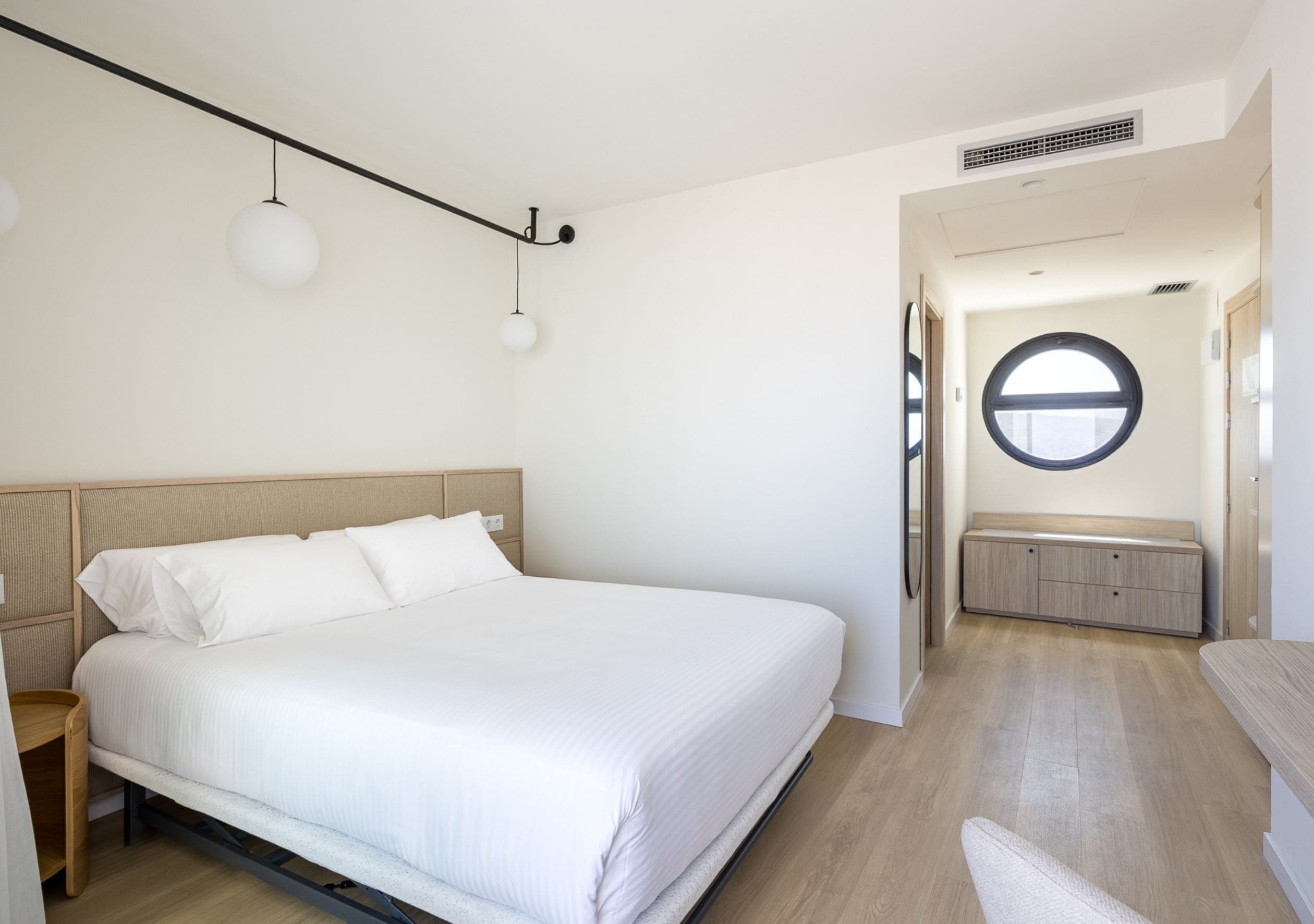 Un dormitorio moderno con una cama grande, un ventanal redondo y un banco empotrado.