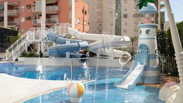 Parque acuático con toboganes y una piscina, rodeado de edificios.