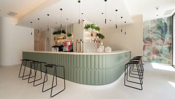 Un bar moderno con una barra curva, varios taburetes, plantas colgantes y un amplio ventanal con vistas.