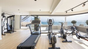 Un gimnasio moderno en casa con cinta de correr, elíptica y bicicleta estática, con vistas a un paisaje marino.
