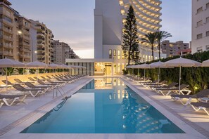 Una piscina al aire libre, sombrillas, sillones reclinables de piscina
