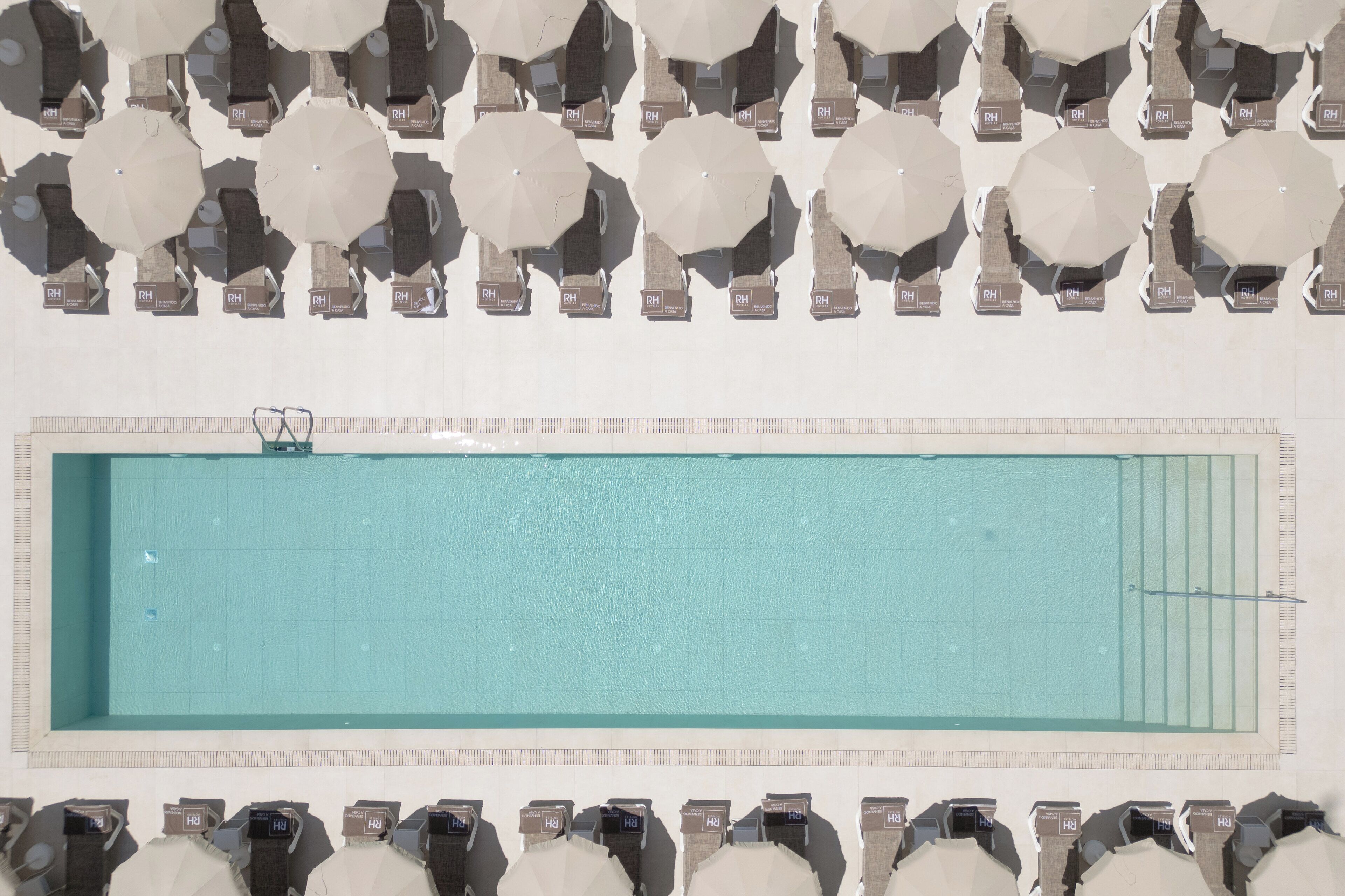 A pool with multiple umbrellas and lounge chairs arranged around it.