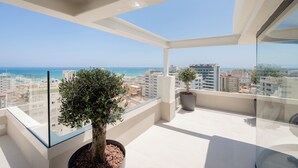 Un balcón con barandilla de vidrio, plantas en macetas y una vista despejada de la ciudad y el mar.