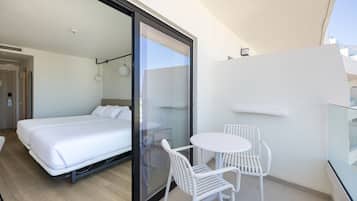 Une chambre d’hôtel moderne, équipée d’un lit, d’une porte vitrée donnant sur un balcon et d’une petite table avec des chaises.