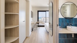 Habitación de hotel moderna con un ventanal grande, un espejo redondo, un lavabo blanco y un armario de madera.