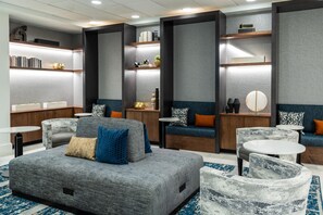A modern lounge area with seating, a coffee table, and a bookshelf. - Hilton Garden Inn Arlington/Courthouse Plaza (Arlington)