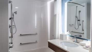 Un baño moderno con cabina de ducha a ras de suelo, tocador con lavabo y un espejo grande.