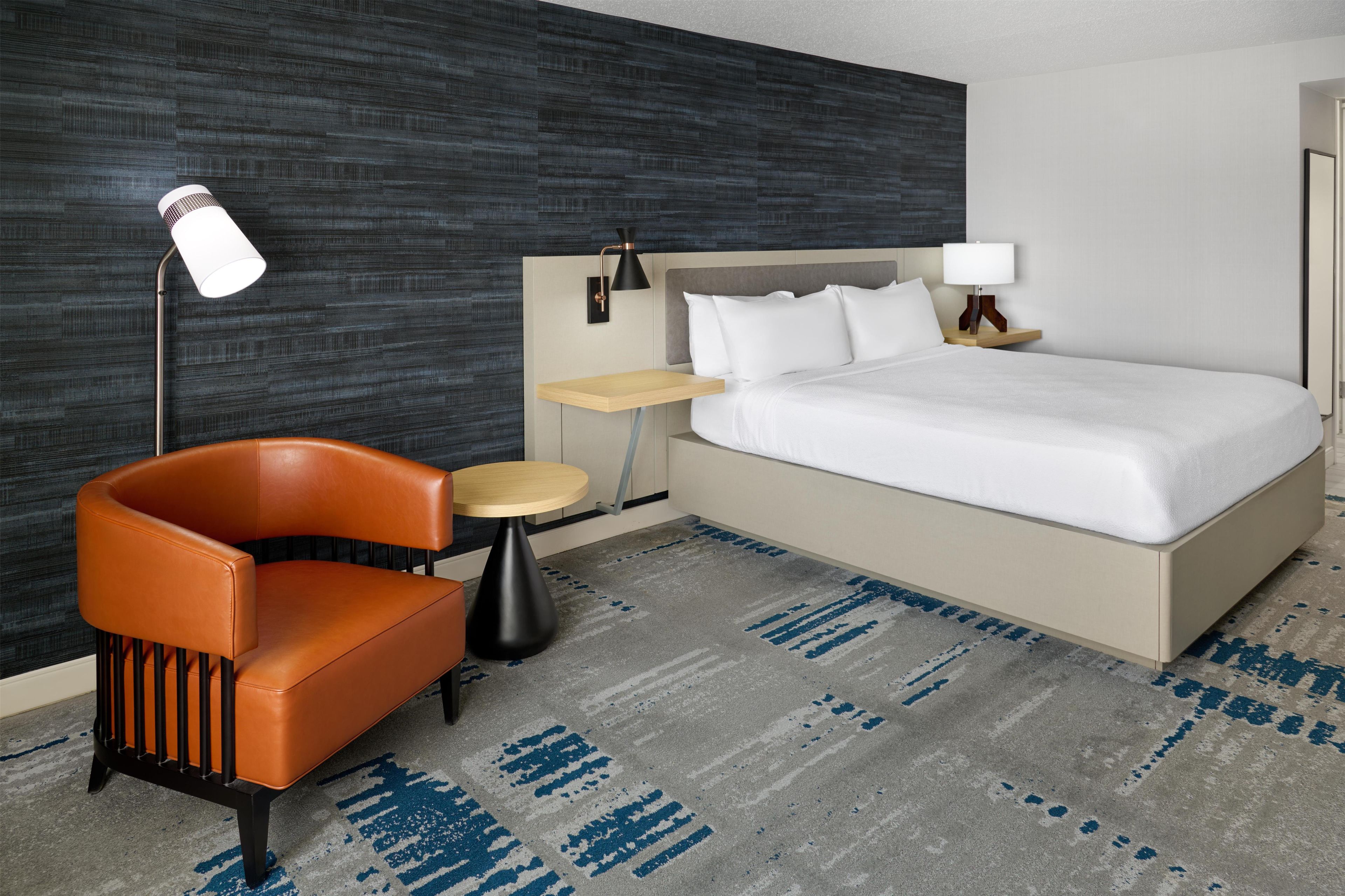 Una habitación de hotel con una cama, una silla, una mesita y una lámpara.