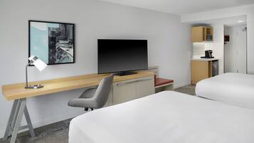 Habitación de hotel con cama, escritorio con computadora, televisión, silla y kitchenette.