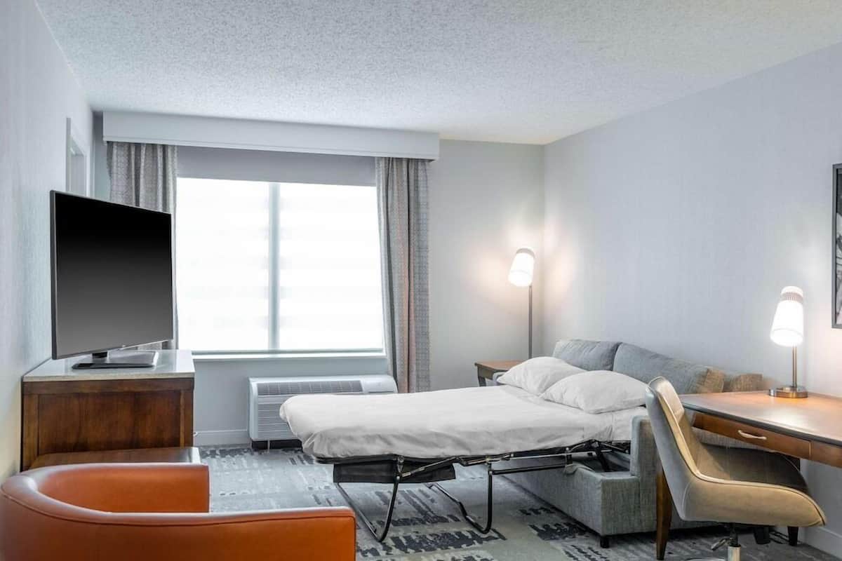 A hotel room with a bed, a desk, a chair, a TV, and a window.