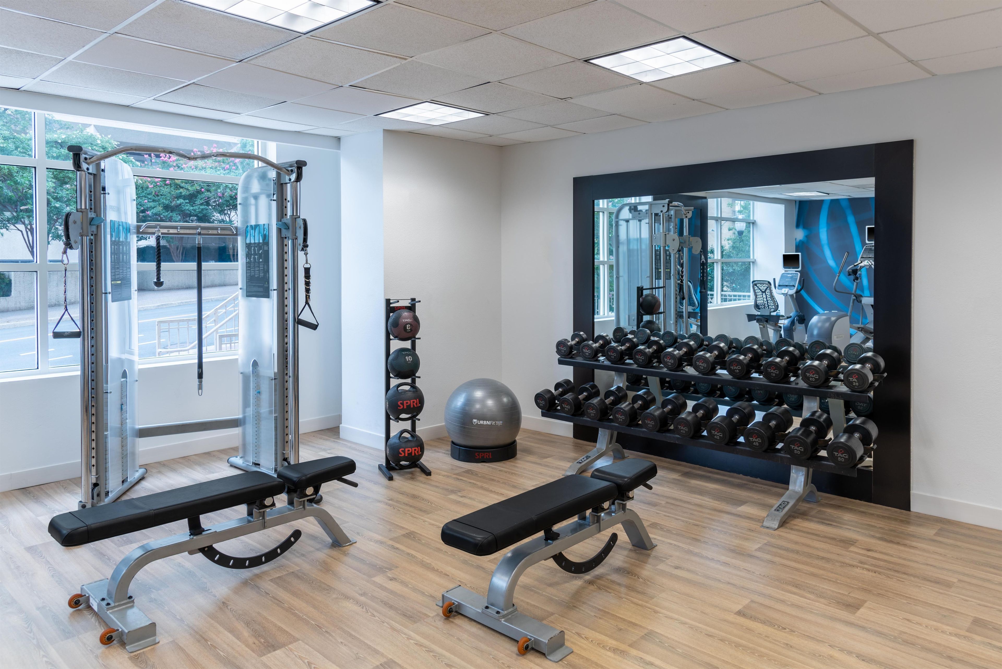A gym with exercise equipment, a bench, a rack of dumbbells, and a large mirror.