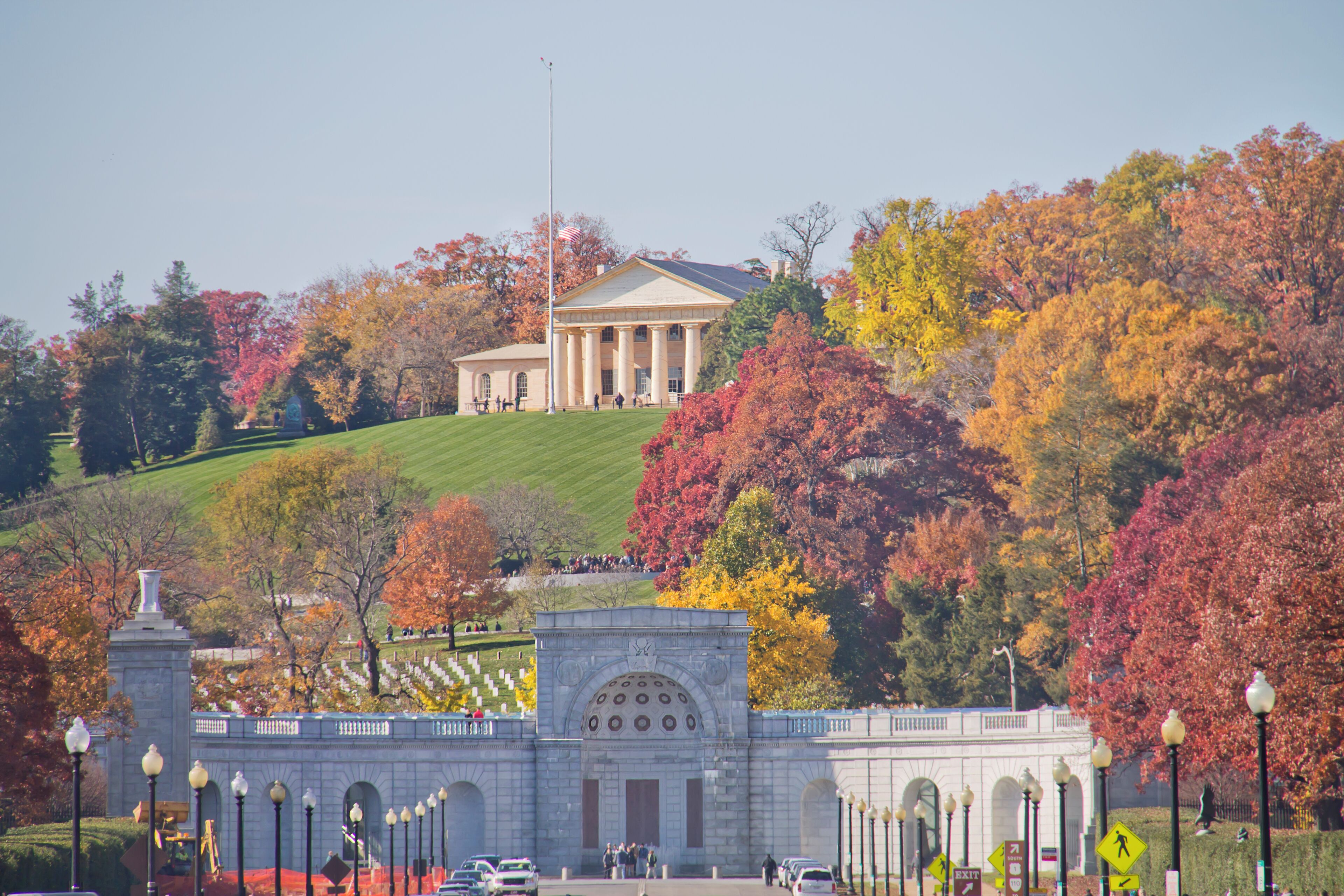 A large building with a classical architectural style, surrounded by a well-maintained lawn and a variety of trees with autumn foliage.