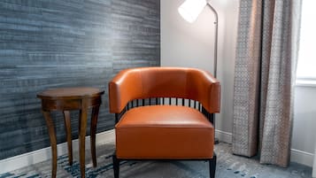 Una habitación con una silla moderna, una pequeña mesa de madera, una lámpara de pie y cortinas estampadas.
