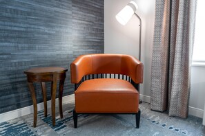 A room with a modern chair, a small wooden table, a floor lamp, and patterned curtains. - Hilton Garden Inn Arlington/Courthouse Plaza (Arlington)