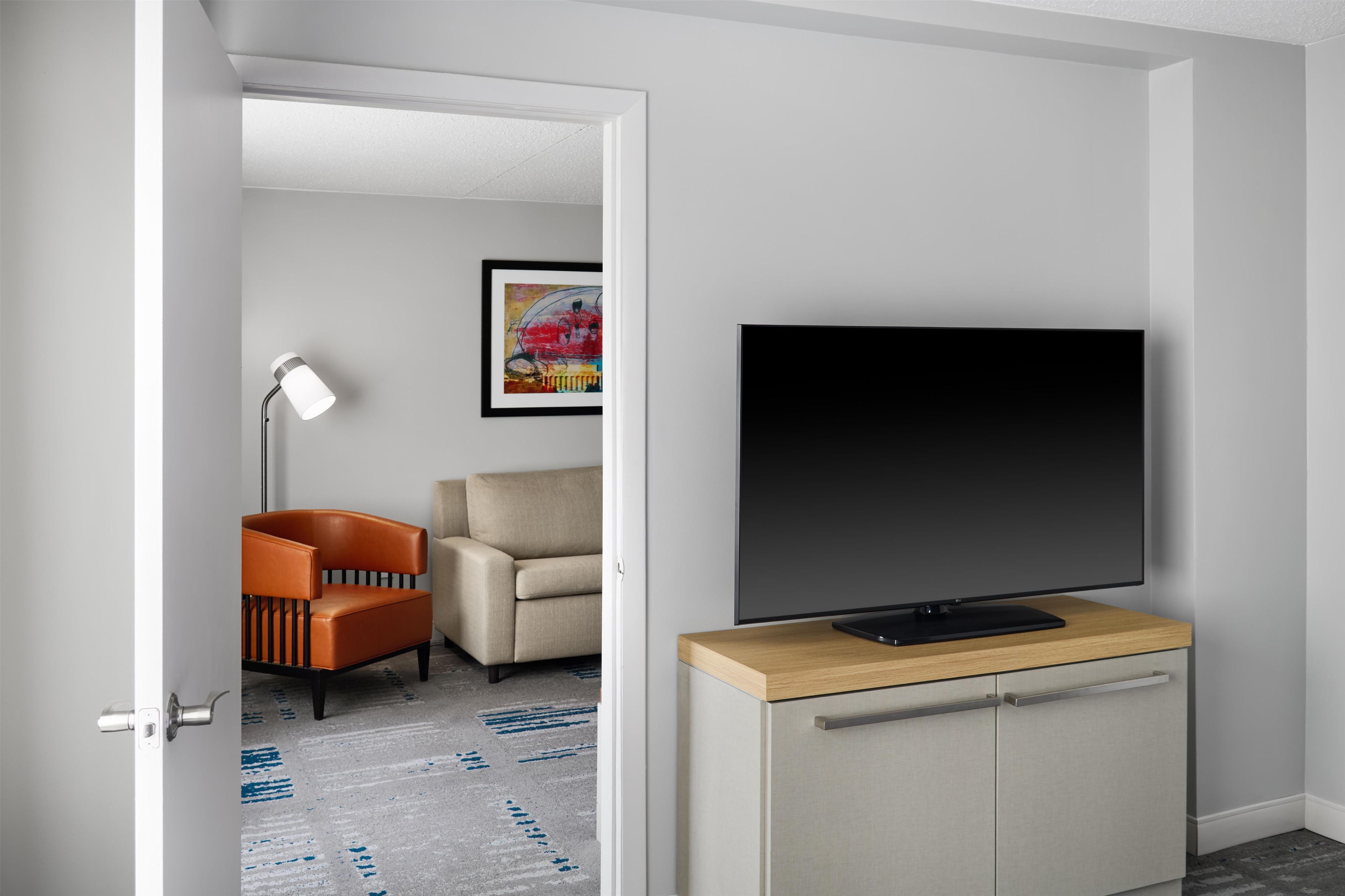 Ein modernes Wohnzimmer mit Flachbildfernseher auf einem Holzschrank, einem beigen Sofa, einem orangefarbenen Sessel und einer Stehlampe.