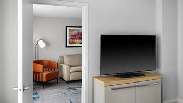 Ein modernes Wohnzimmer mit Flachbildfernseher auf einem Holzschrank, einem beigen Sofa, einem orangefarbenen Sessel und einer Stehlampe.