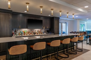 A bar area with a long counter, multiple stools, and a variety of bottles. - Hilton Garden Inn Arlington/Courthouse Plaza (Arlington)