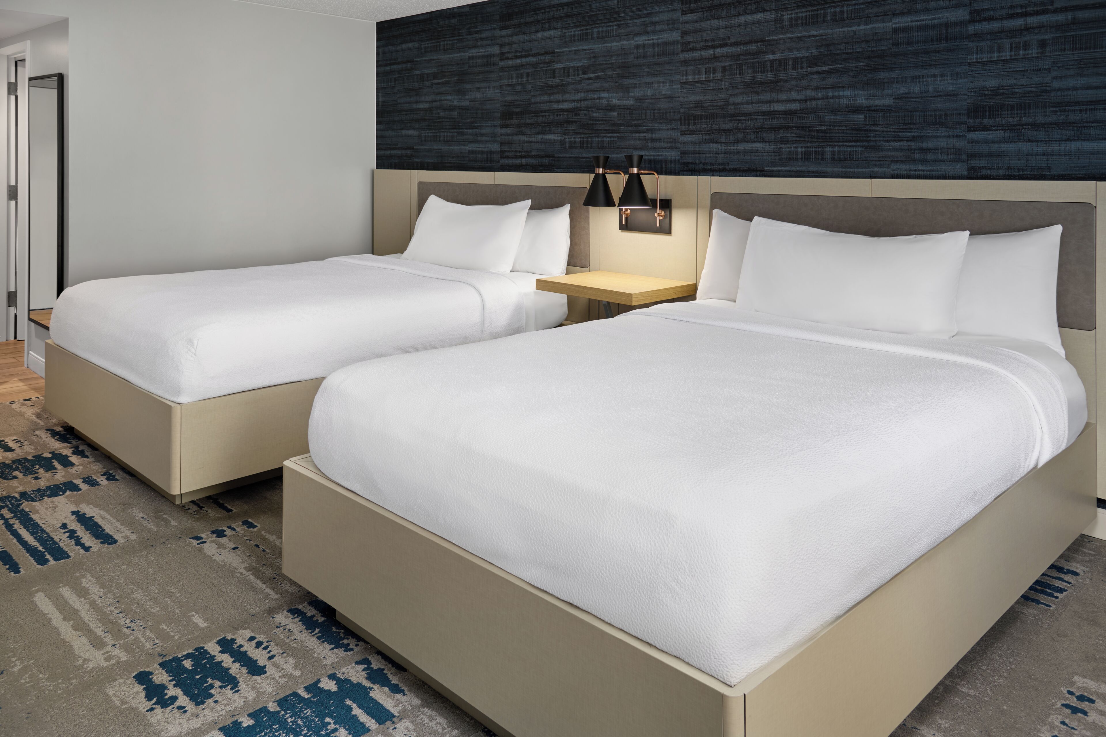 Una habitación de hotel con dos camas, una mesita de noche y una lámpara de pared.