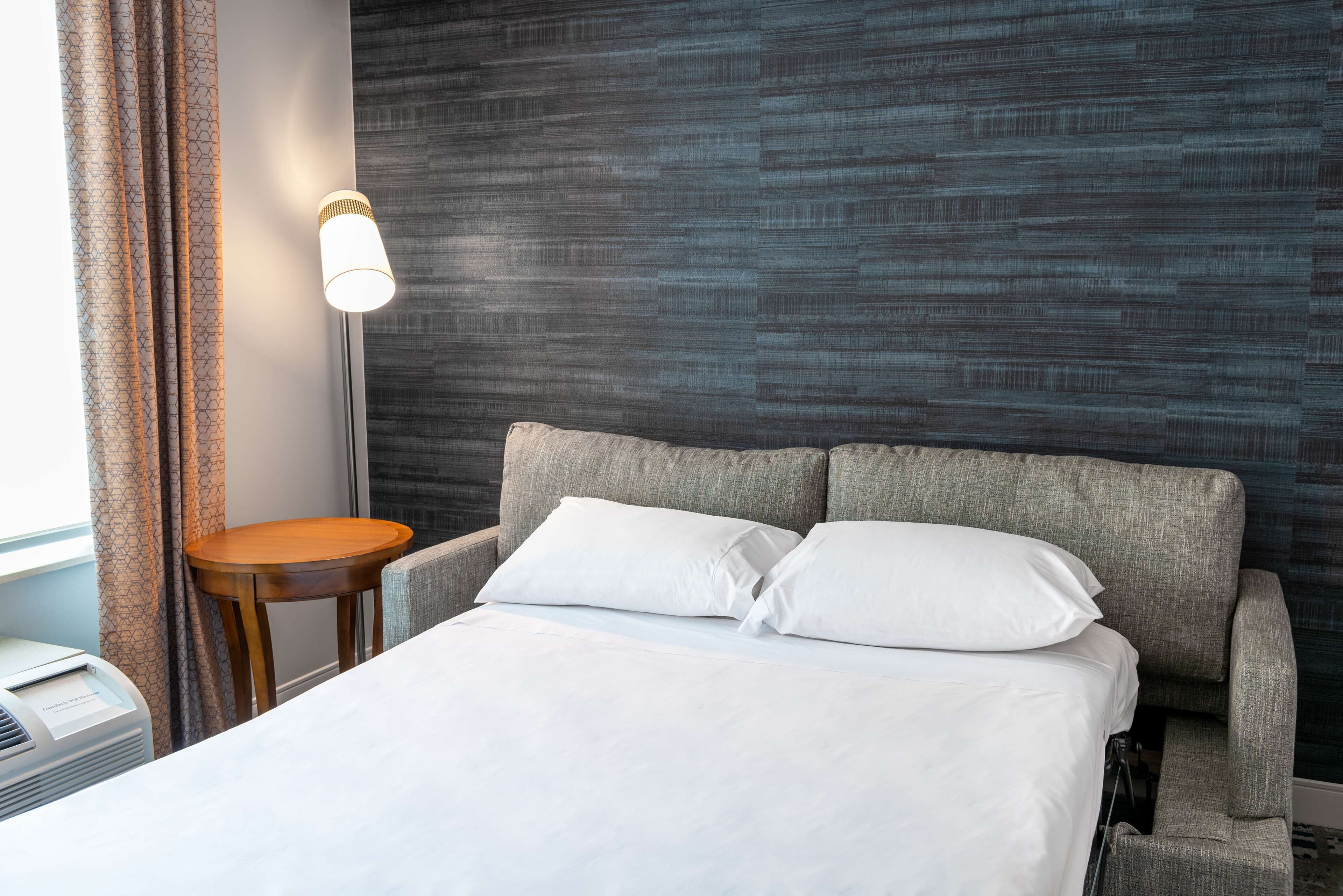 Una habitación de hotel con una cama, una mesita de noche, una lámpara y una pared con un diseño texturizado.