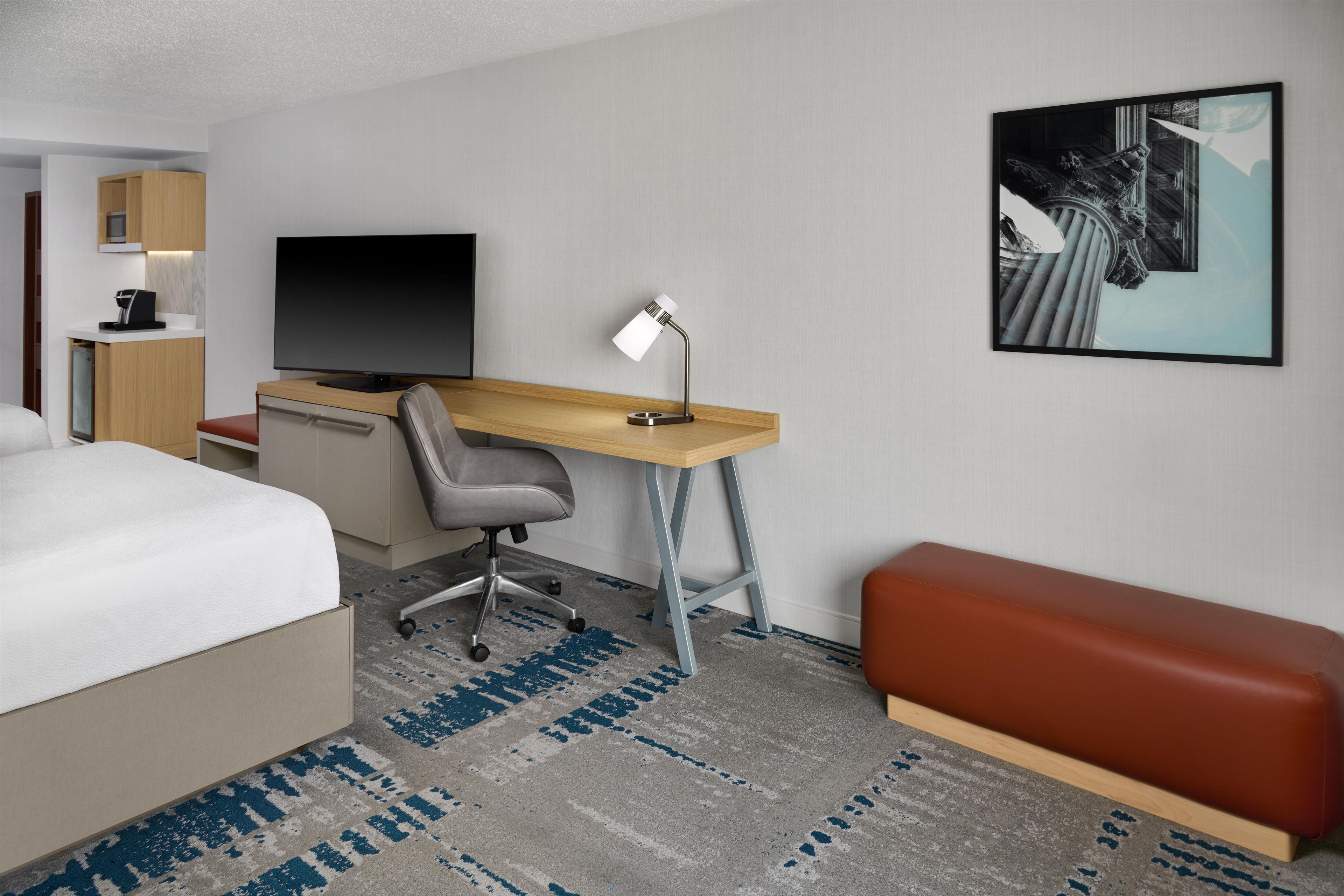 Une chambre d’hôtel avec un lit, un bureau, une chaise et un tableau au mur.