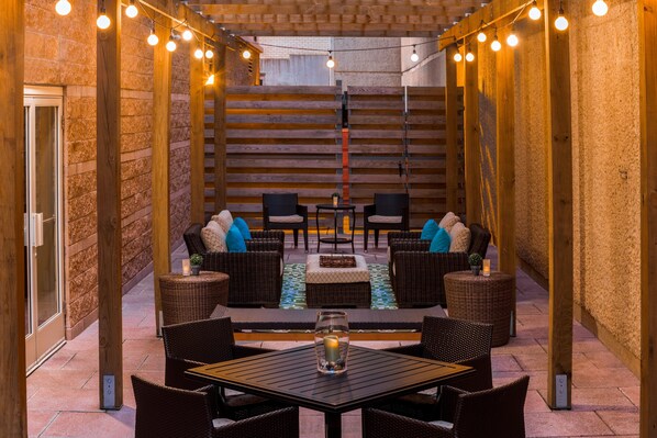 Un patio al aire libre con muebles de mimbre, una mesa y luces colgantes.