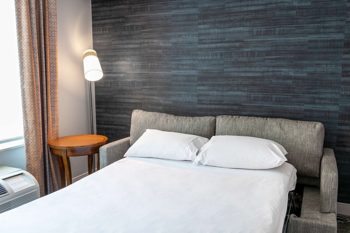 A hotel room with a bed, a bedside table, a lamp, and a wall with a textured pattern.