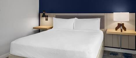 A hotel room with a bed, two bedside tables, a nightstand, and a wall-mounted lamp.