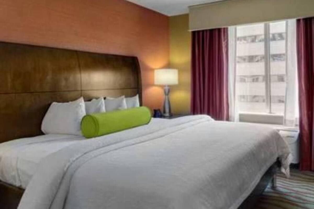 A hotel room with a large bed, a headboard, a window with curtains, and a lamp.