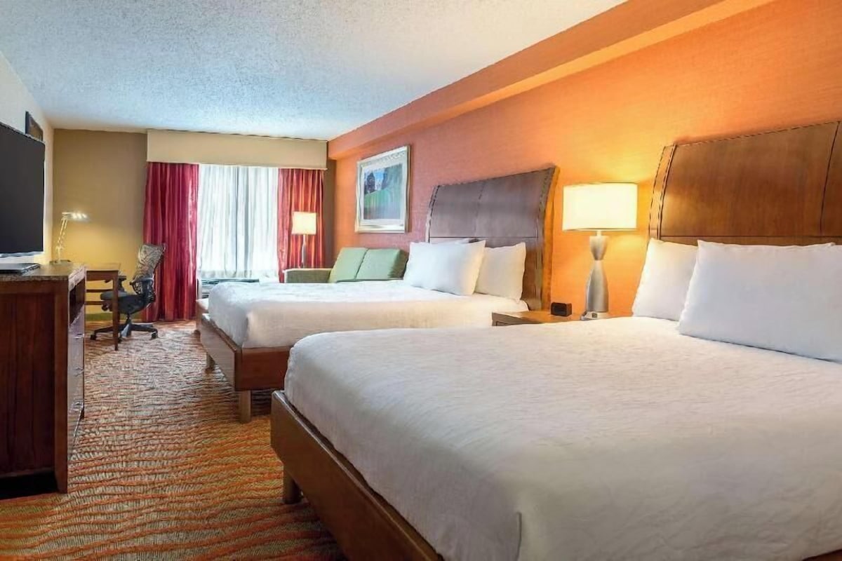 A hotel room with two beds, a desk, a chair, and a television.