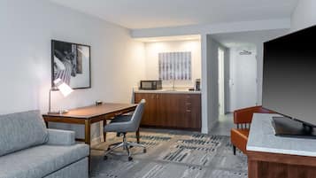 Una habitación moderna con sofá, escritorio, silla, televisión y una zona de cocina con microondas, además de una alfombra estampada.