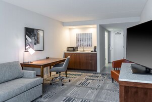 Una habitación moderna con sofá, escritorio, silla, televisión y una zona de cocina con microondas, además de una alfombra estampada.