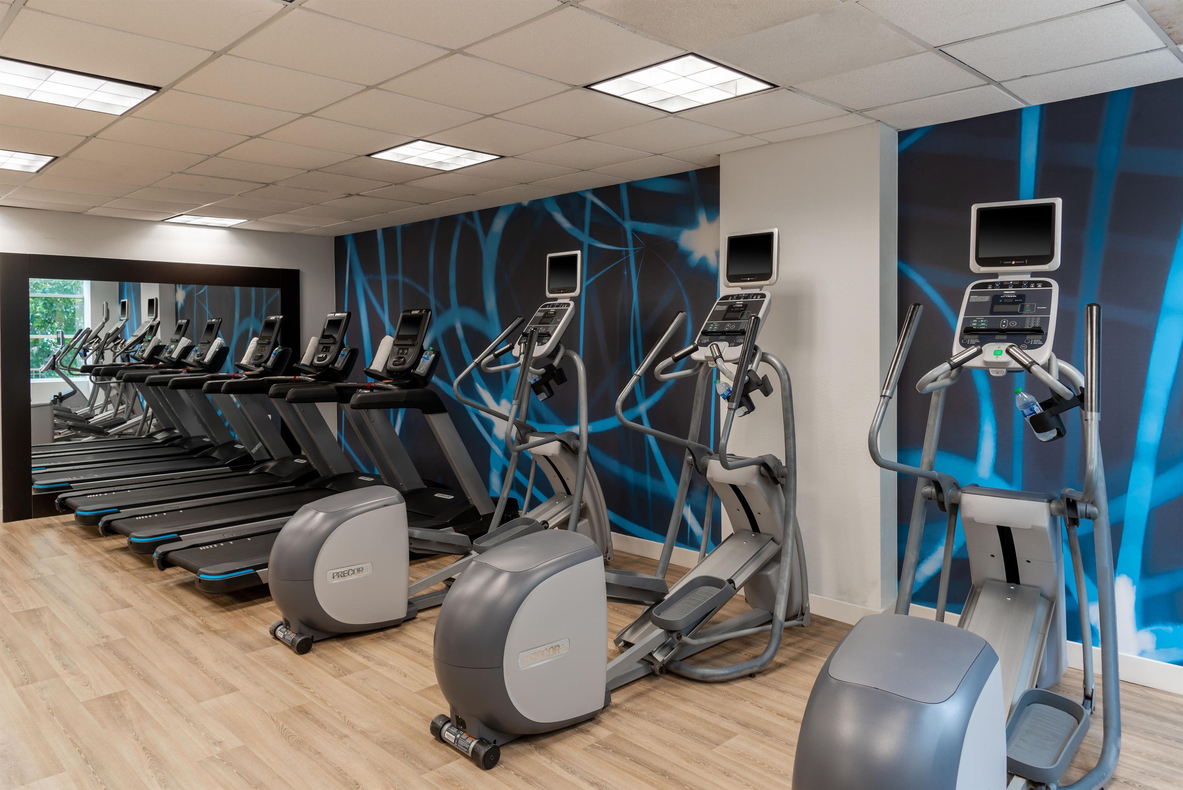 Un gimnasio con varias cintas de correr, elípticas y una bicicleta estática de pared.