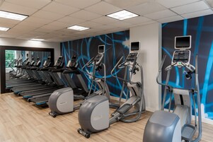 Een sportschool met meerdere loopbanden, elliptische trainers en een vastgezet hometrainer.