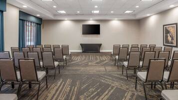 A conference room with rows of chairs, a flat-screen TV on the wall, and a carpeted floor.
