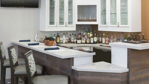 A modern kitchen with white cabinetry, a built-in bar area with stools, and a variety of bottles.