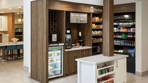 A coffee shop with a refrigerated display case, a coffee machine, and shelves stocked with snacks and beverages.