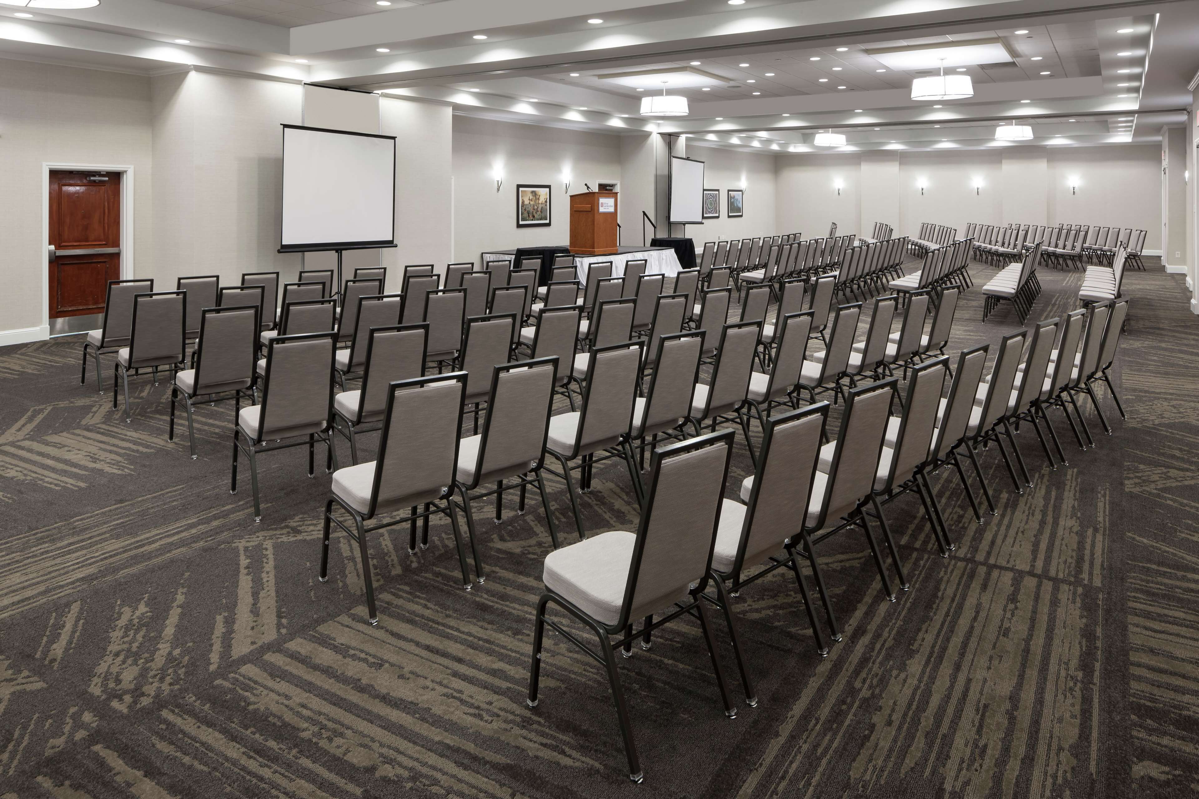 A conference room with rows of chairs, a projector screen, and a podium.